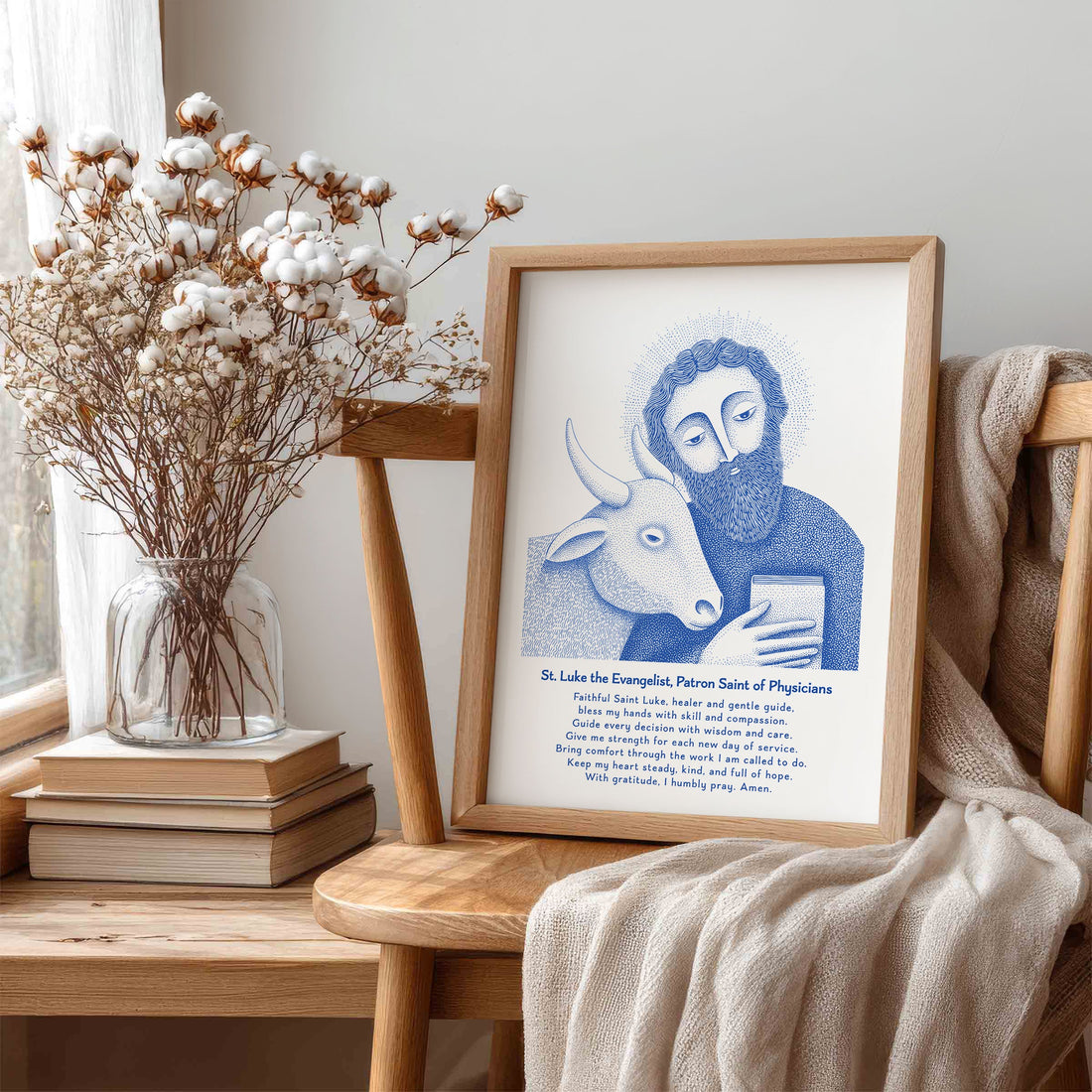 Blue St. Luke prayer art print in a wooden frame beside cotton branches and books