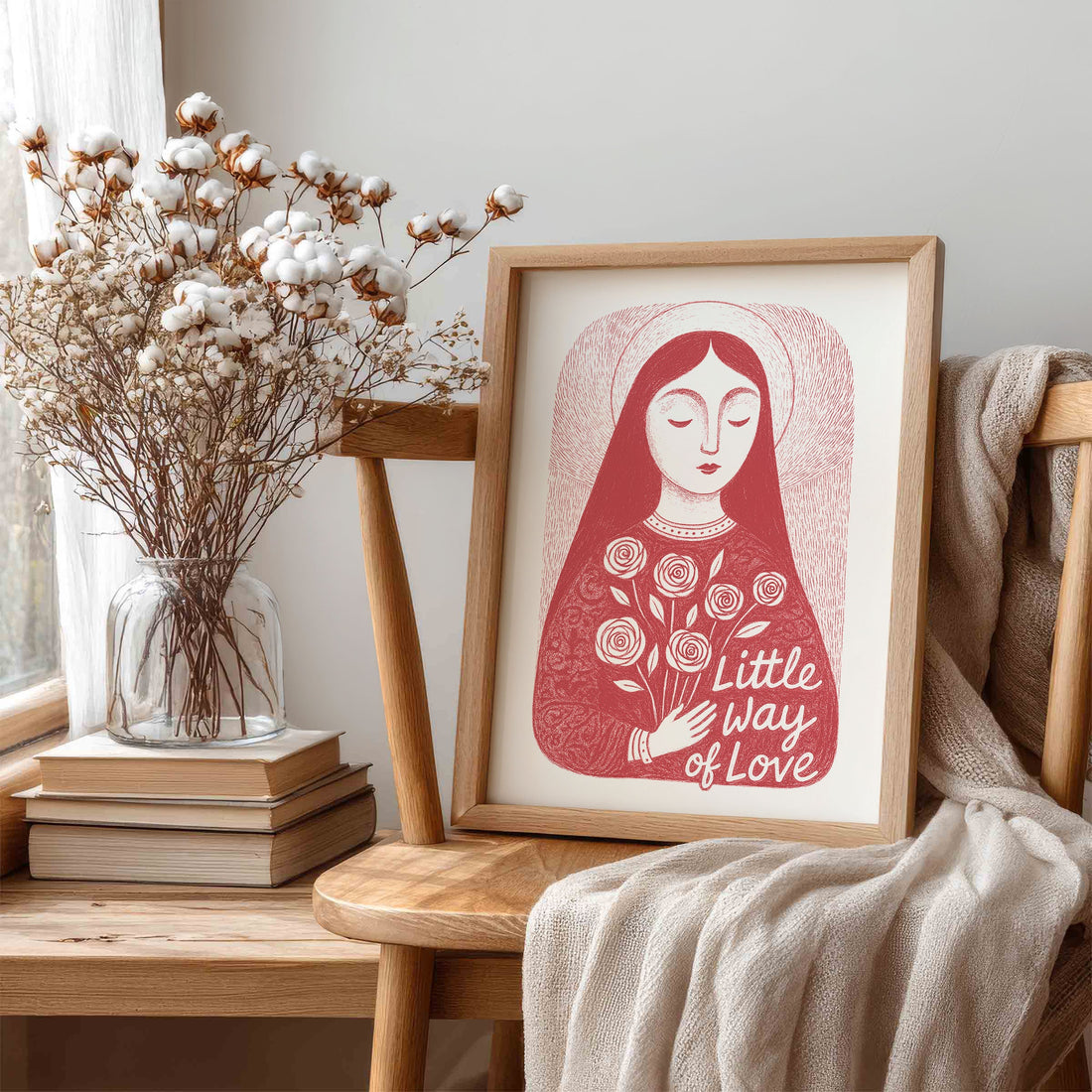 Framed red St. Therese print on a chair beside cotton branches and books