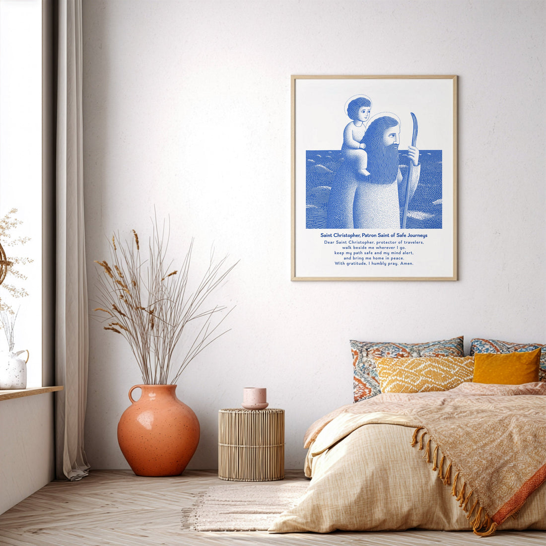 Blue St. Christopher prayer print in a wooden frame beside a bed and a terracotta vase.