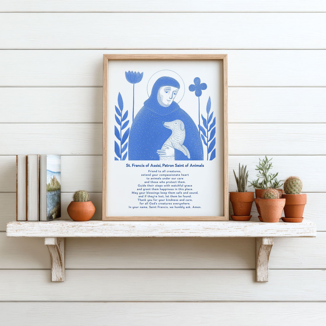 Blue St. Francis of Assisi with dog art print displayed on a white shelf with small plants