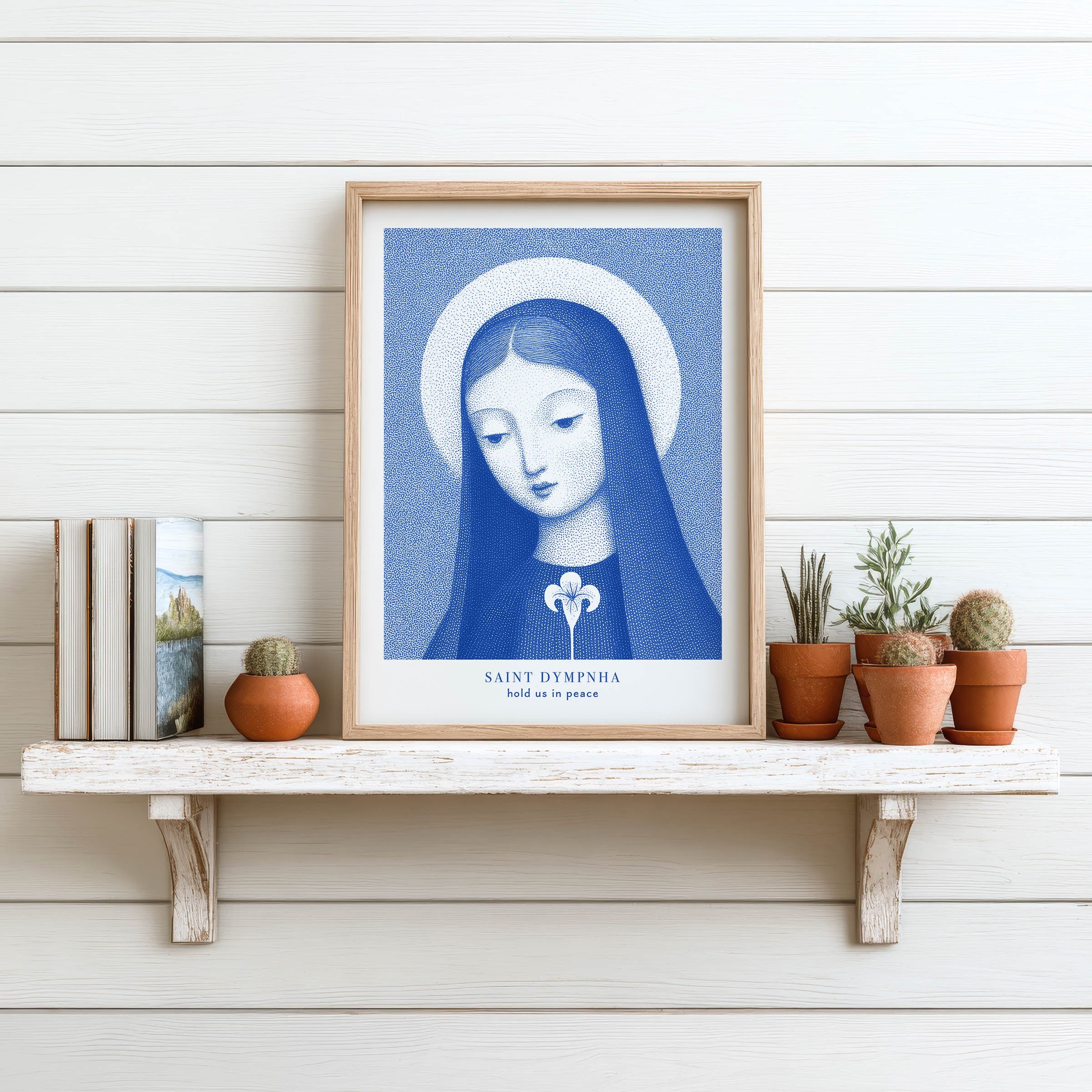 Blue St. Dymphna art print with a lily and the words hold us in peace, displayed on a white shelf