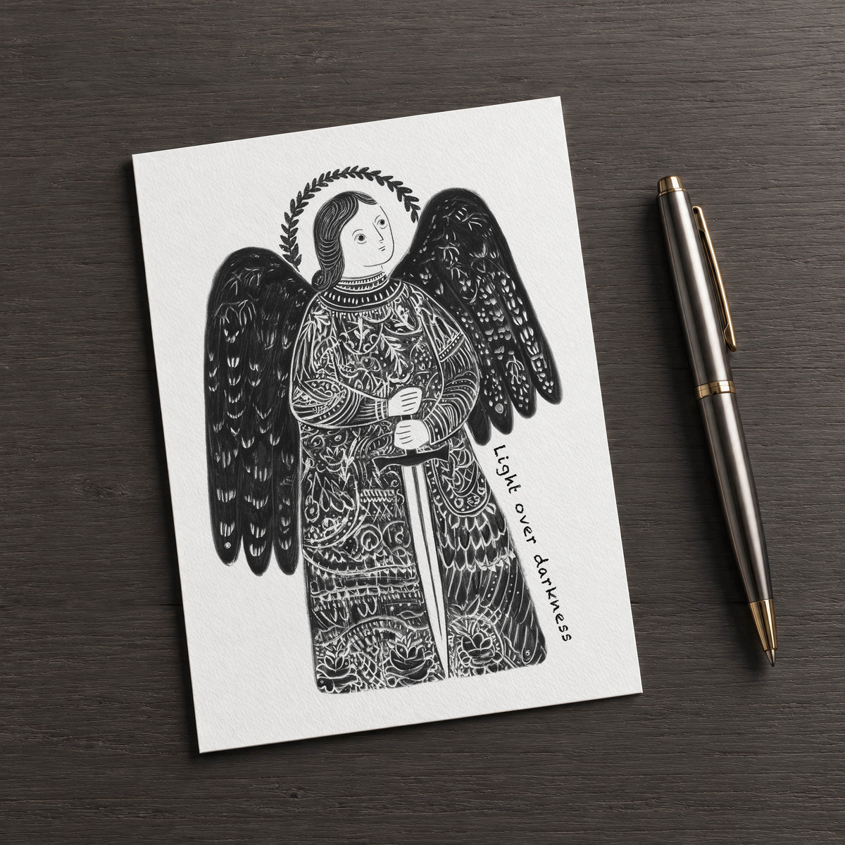 Black St Michael the Archangel card on a dark table beside a pen