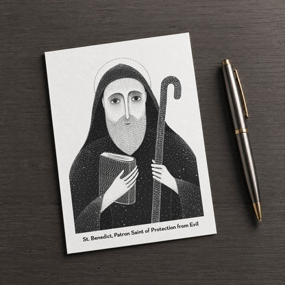 Black St Benedict card on a dark table beside a pen