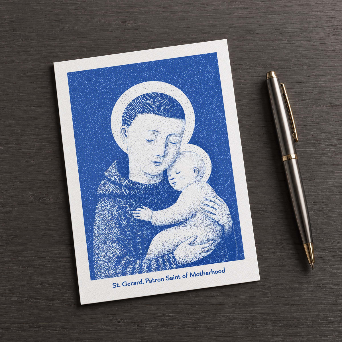 Blue St Gerard Majella card on a dark table beside a pen