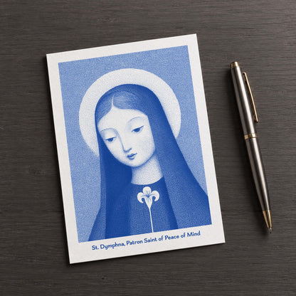 Blue St Dymphna card on a dark table beside a pen