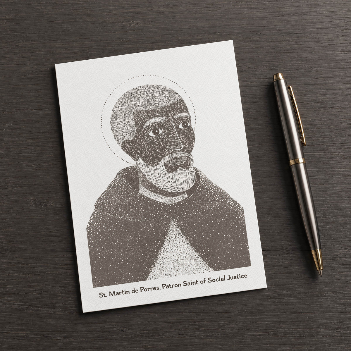 Brown St Martin de Porres card on a dark table beside a pen