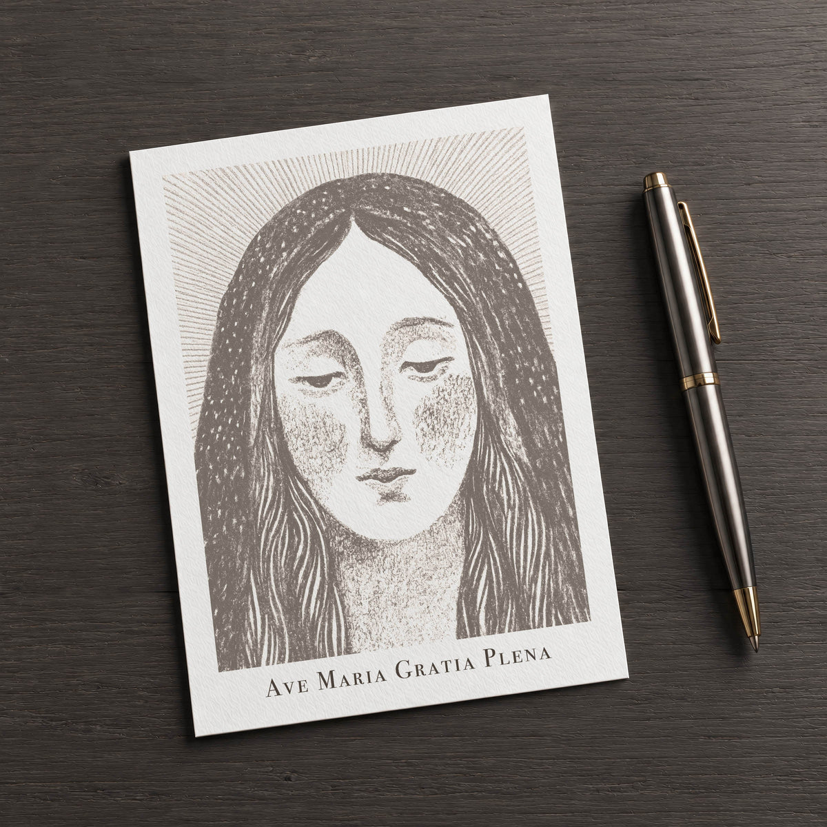 Brown Virgin Mary card on a dark table beside a pen