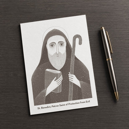 Brown St Benedict card on a dark table beside a pen