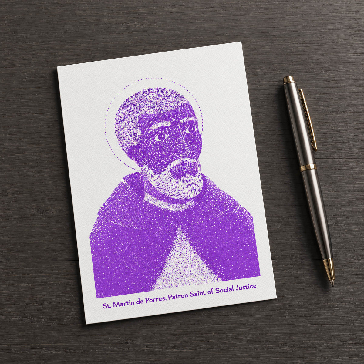 Purple St Martin de Porres card on a dark table beside a pen