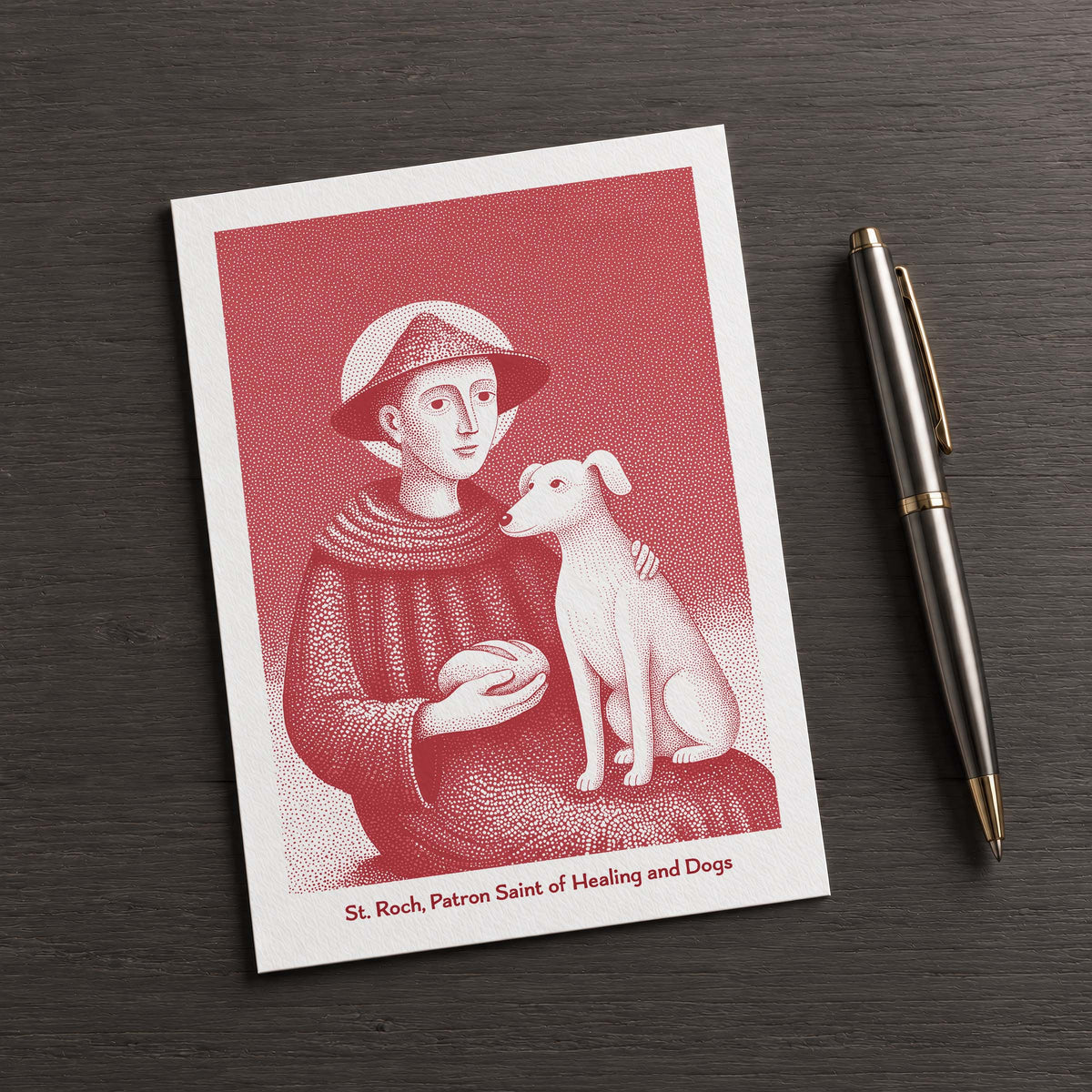 Red St Roch card on a dark table beside a pen