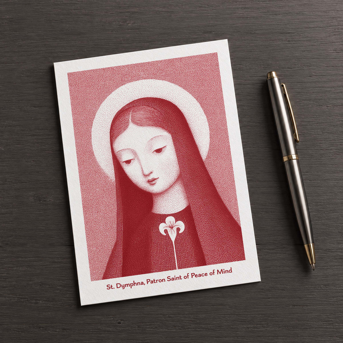 Red St Dymphna card on a dark table beside a pen