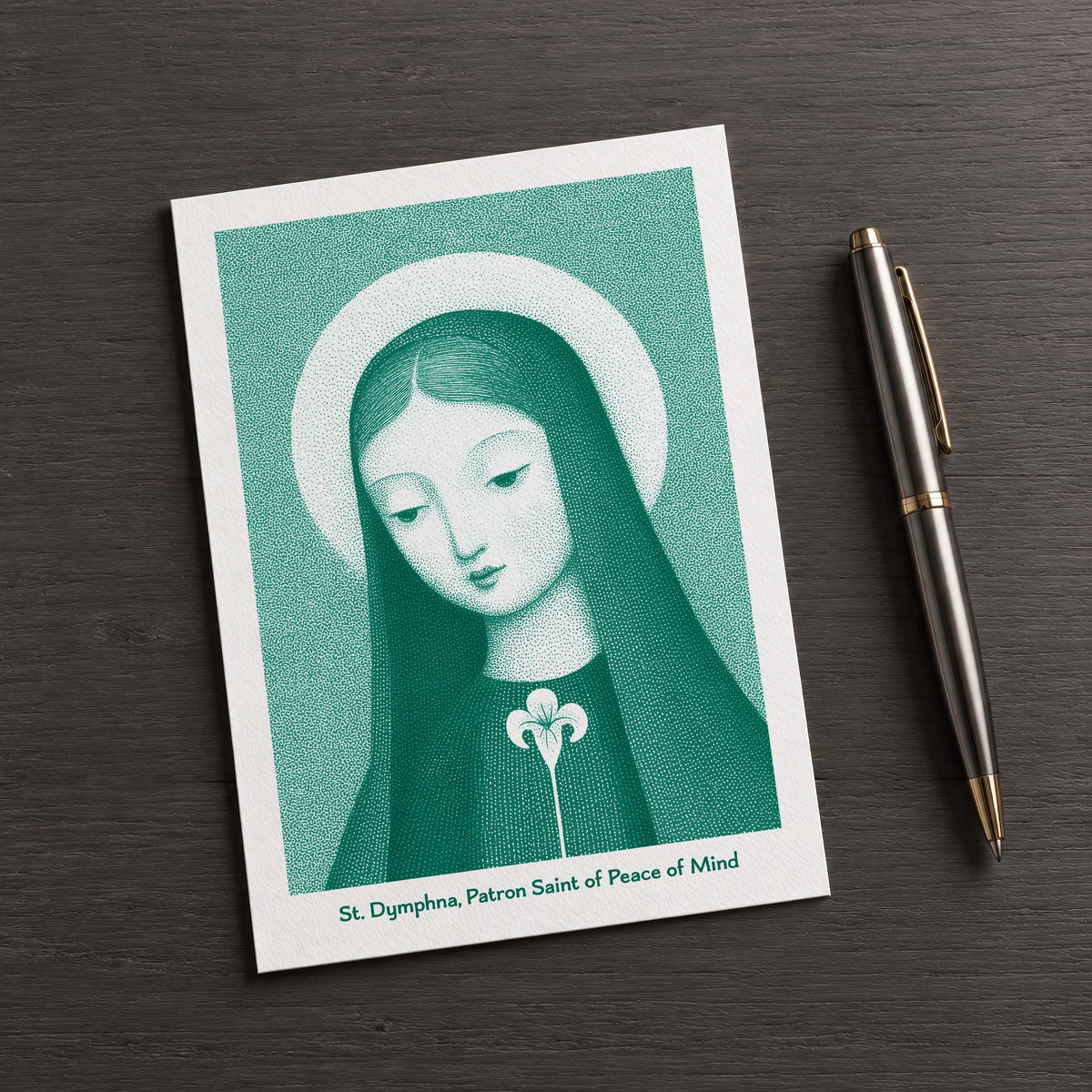 Teal St Dymphna card on a dark table beside a pen