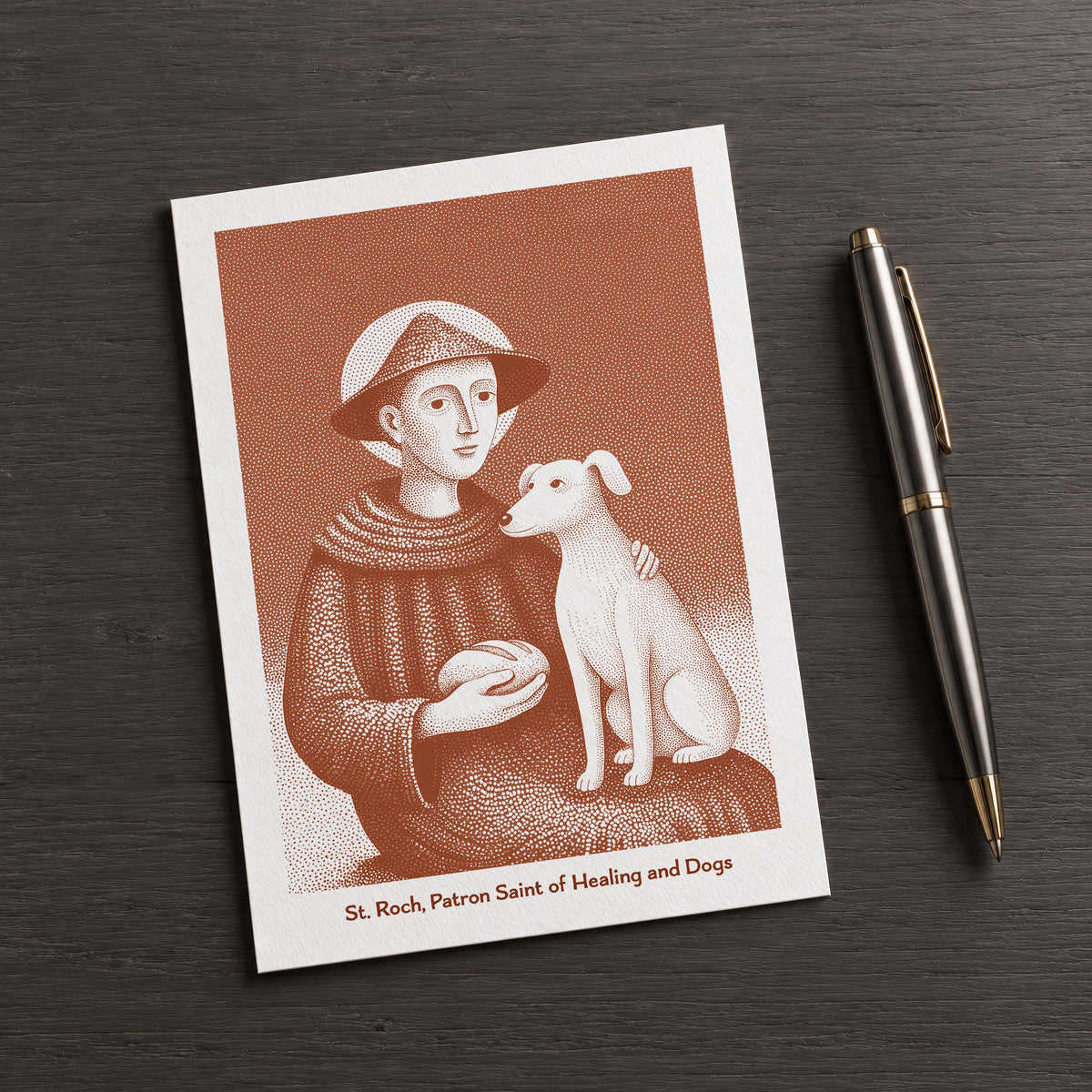 Terracotta St Roch card on a dark table beside a pen