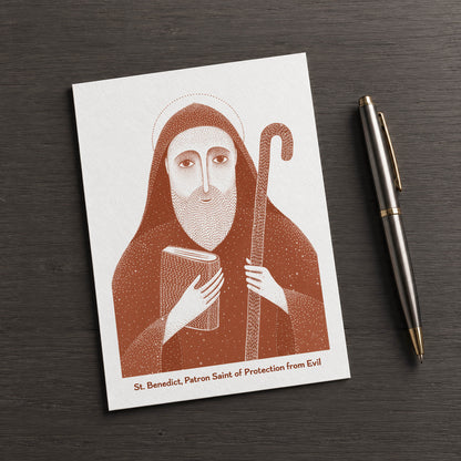 Terracotta St Benedict card on a dark table beside a pen